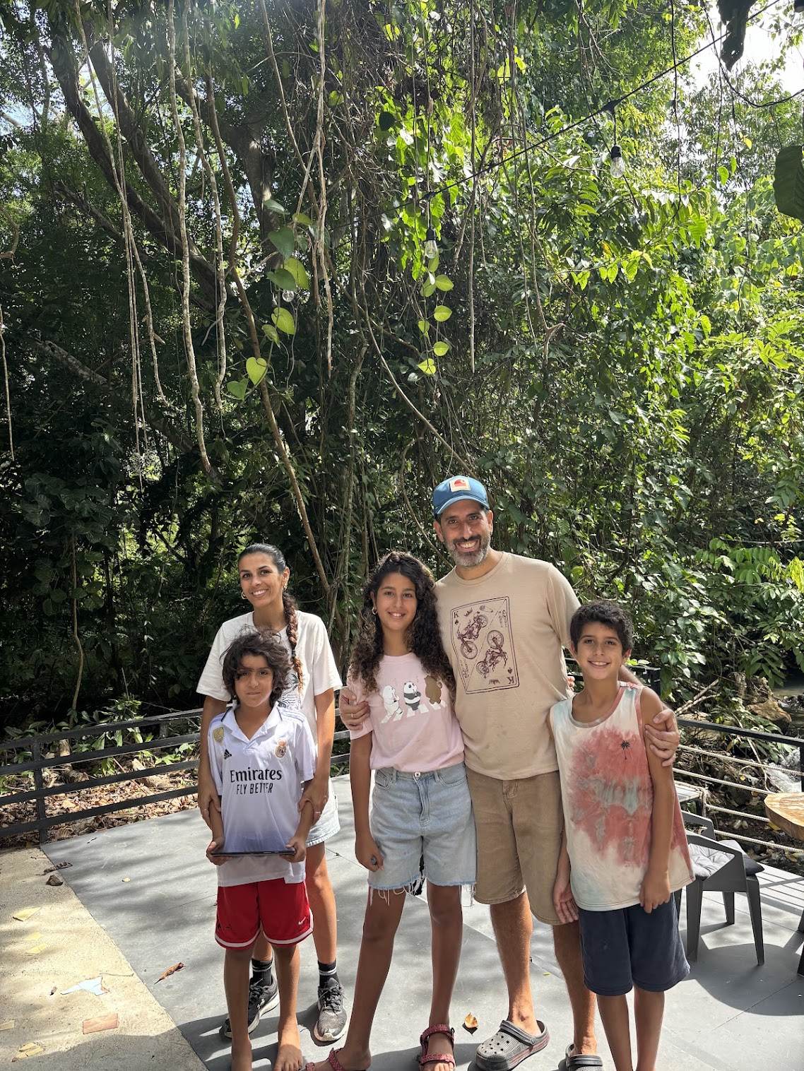 Shay, Shani and their three kids Romy, Rafaeli, and Rani standing on the deck at MediJungle with jungle vines hanging behind them