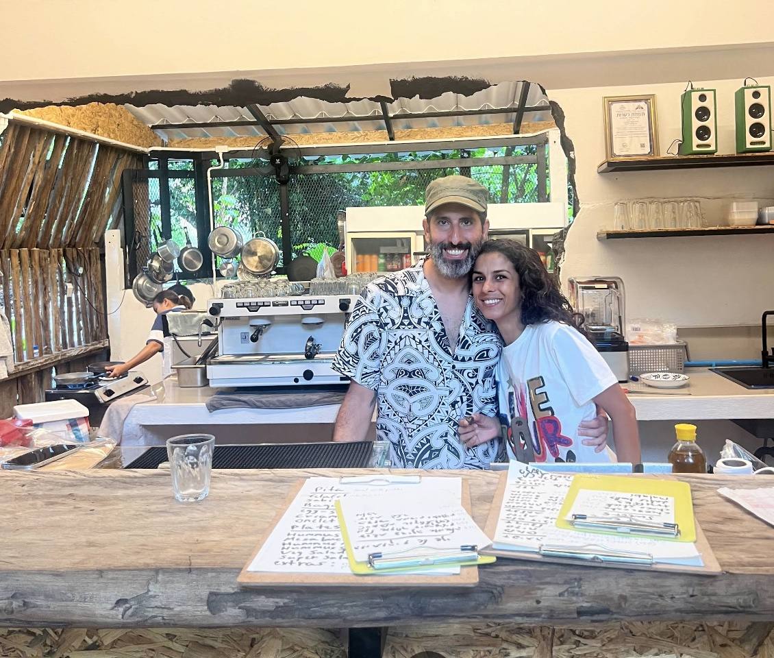 Shay and Shani at the MediJungle bar, smiling, handwritten menu papers in front of them